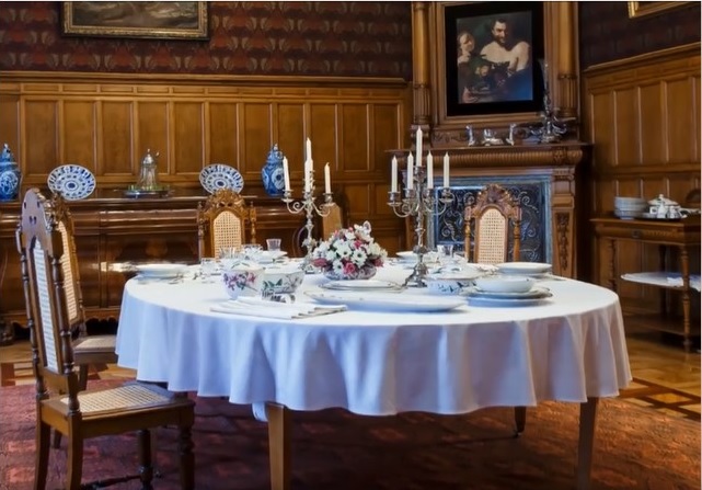 zdjęcie przedstawia stół na środku pokoju otoczony krzesłami. Na stole znajduje się zastawa stołowa.