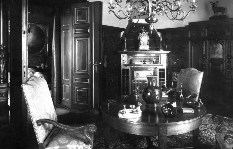 czarno-białe zdjęcie przedstawia okrągły stół. Wokół stołu dwa krzesła. W rogu pomieszczenia znajduje się kominek.