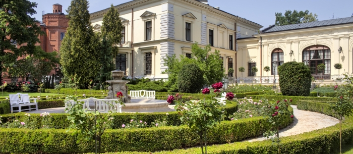 A bright, multi-story palace with a French garden, low hedges, and a fountain in the foreground.