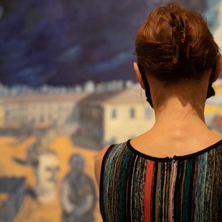 Na pierwszym planie odwrócona tyłem kobieta. Stoi przed obrazem