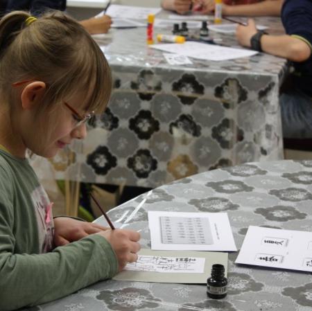 Uczestniczka warsztatów kaligrafuje litery japońskiego alfabetu.