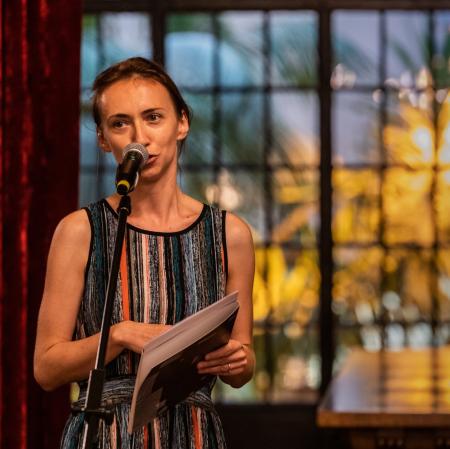 Kobieta mówiąca do mikrofonu. Widoczna od pasa w górę