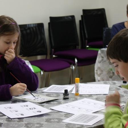 Uczestnicy warsztatów kaligrafują litery japońskiego alfabetu.