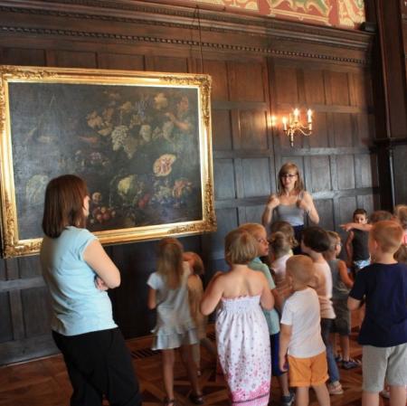 Uczestnicy warsztatów Pałacowa menażeria na sali balowej w Muzeum Pałac Herbsta szukają zwierzątek na obrazie Giovanniego Battisty Ruoppolo "Alegoria zbiorów jesiennych".