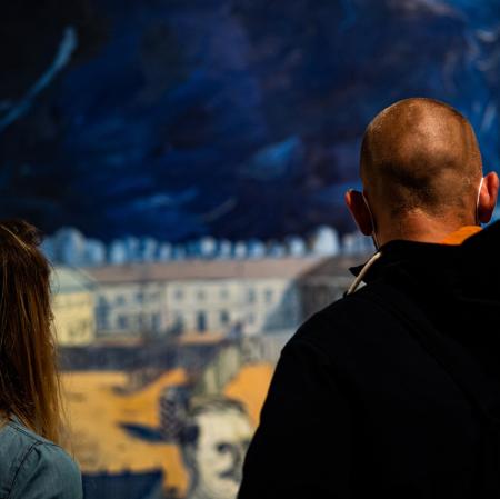 Dwie odwrócone tyłem osoby. Patrzą na widoczny w głębi obraz.