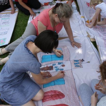 Uczestnicy warsztatów wykonują plan Księżego Młyna na płótnie rozłożonym w przypałacowym ogrodzie.