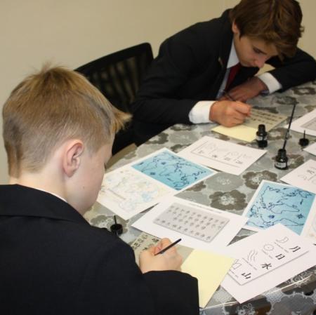 Uczestnicy warsztatów kaligrafują litery japońskiego alfabetu.