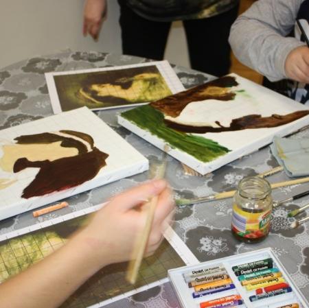 Zbliżenie na dłonie uczestników oraz powstające prace malarskie. Na stole paleta malarska, pędzle, pastele