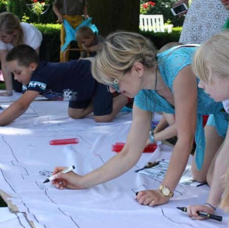 Uczestnicy warsztatów wykonują plan Księżego Młyna na płótnie rozłożonym w przypałacowym ogrodzie.