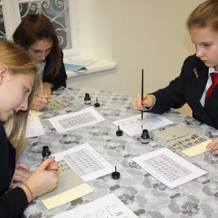 Uczestnicy warsztatów kaligrafują litery japońskiego alfabetu.