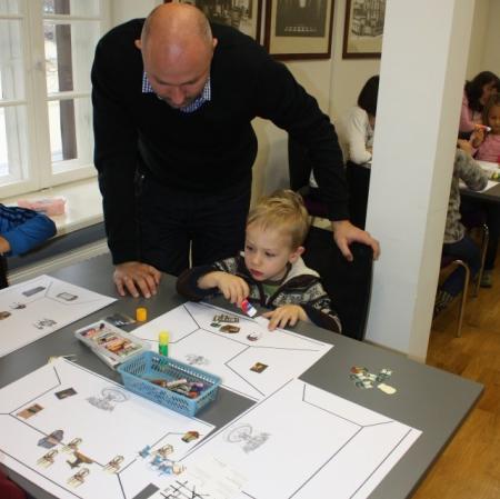 Mały i duży uczestnik warsztatów projektują na szablonie wnętrza wybrany pokój.