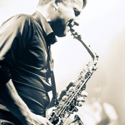 Zdjęcie przedstawia młodego mężczyzny grający na saxofonie