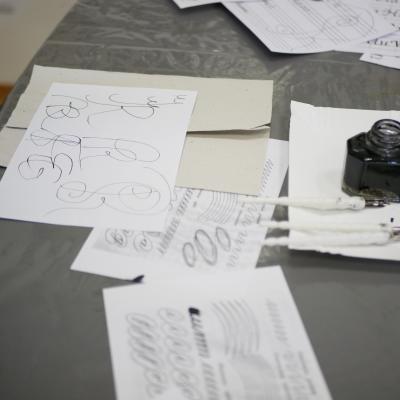 Zdjęcie przedstawia zapisane białe kartki na stole oraz słoiczek z atramentem