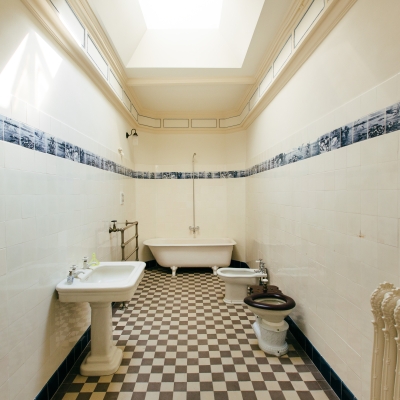 Vintage bathroom with white tiled walls, a blue pattern border, a clawfoot bathtub, and a checkered floor.
