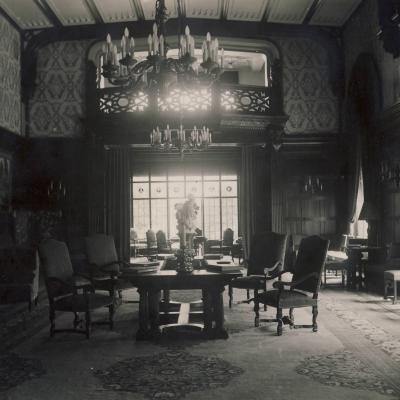 czarno-białe zdjęcie przedstwia wnętrze wilkiej sali, po środku której znajduje się duży stól i krzesła