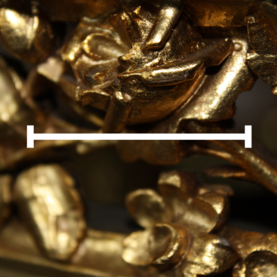 Zbliżenie na złoconą, bogato zdobioną powierzchnię rzeźby lub ornamentu, przedstawiającego stylizowane liście i kwiaty. Na środku obrazu znajduje się pozioma biała linia zakończona krótkimi poprzecznymi kreskami.