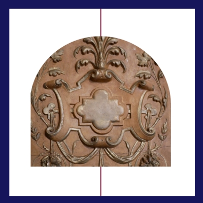 „Dekoracyjny relief w odcieniach terakoty przedstawiający symetryczny, roślinny ornament w stylu klasycznym. Centralnie znajduje się ozdobna rama w kształcie czterolistnej koniczyny, otoczona wijącymi się liśćmi, stylizowanymi łodygami i kwiatowymi motywami. Obraz jest przecięty cienką pionową linią, sugerującą oś symetrii, a całość osadzona jest w granatowej ramce z białym tłem